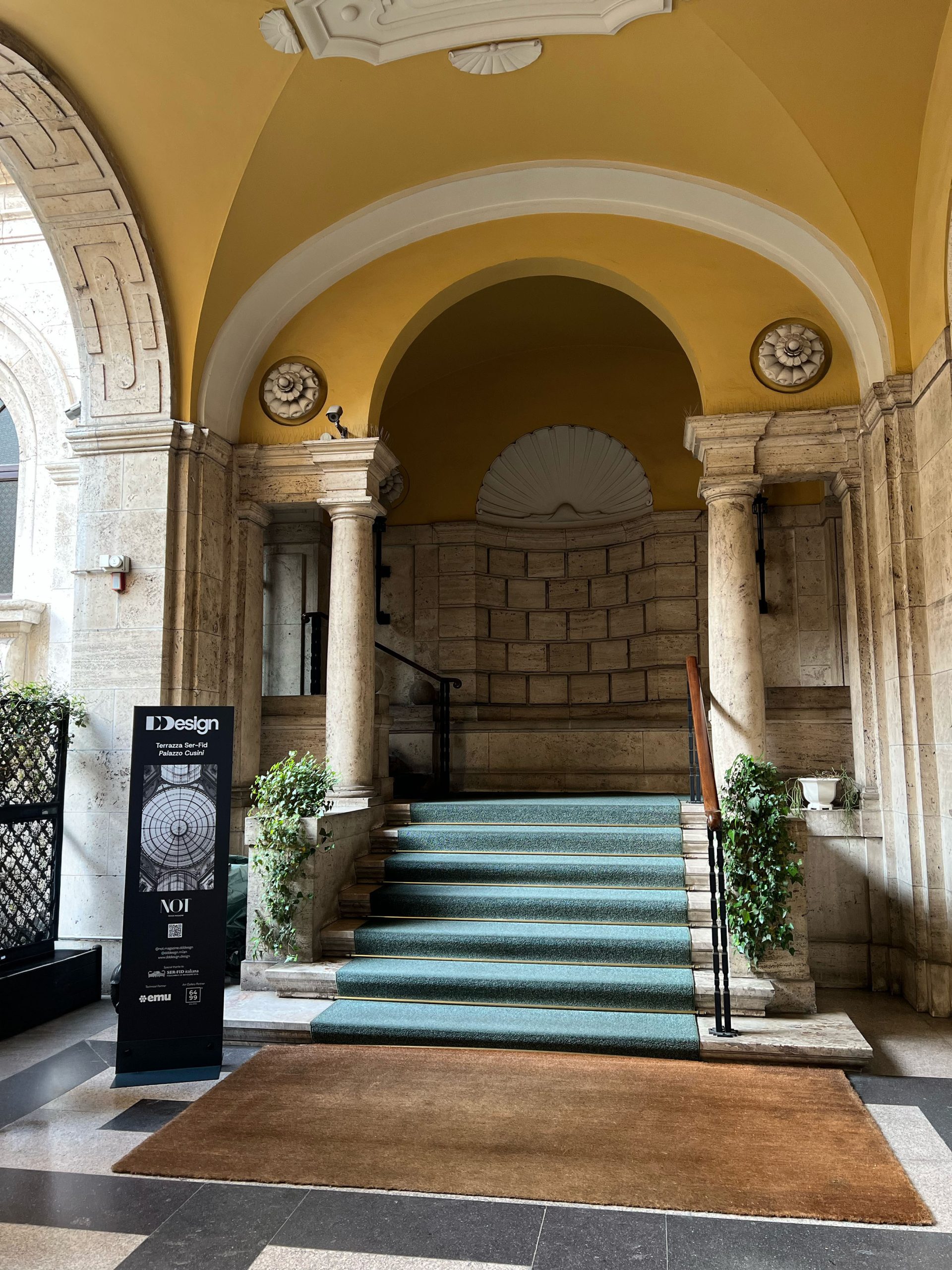 Ingresso elegante con scalinata rivestita in moquette verde, colonne in pietra e soffitto giallo decorato. Design d'interni raffinato, architettura classica italiana. Dettagli di stile e atmosfera accogliente.