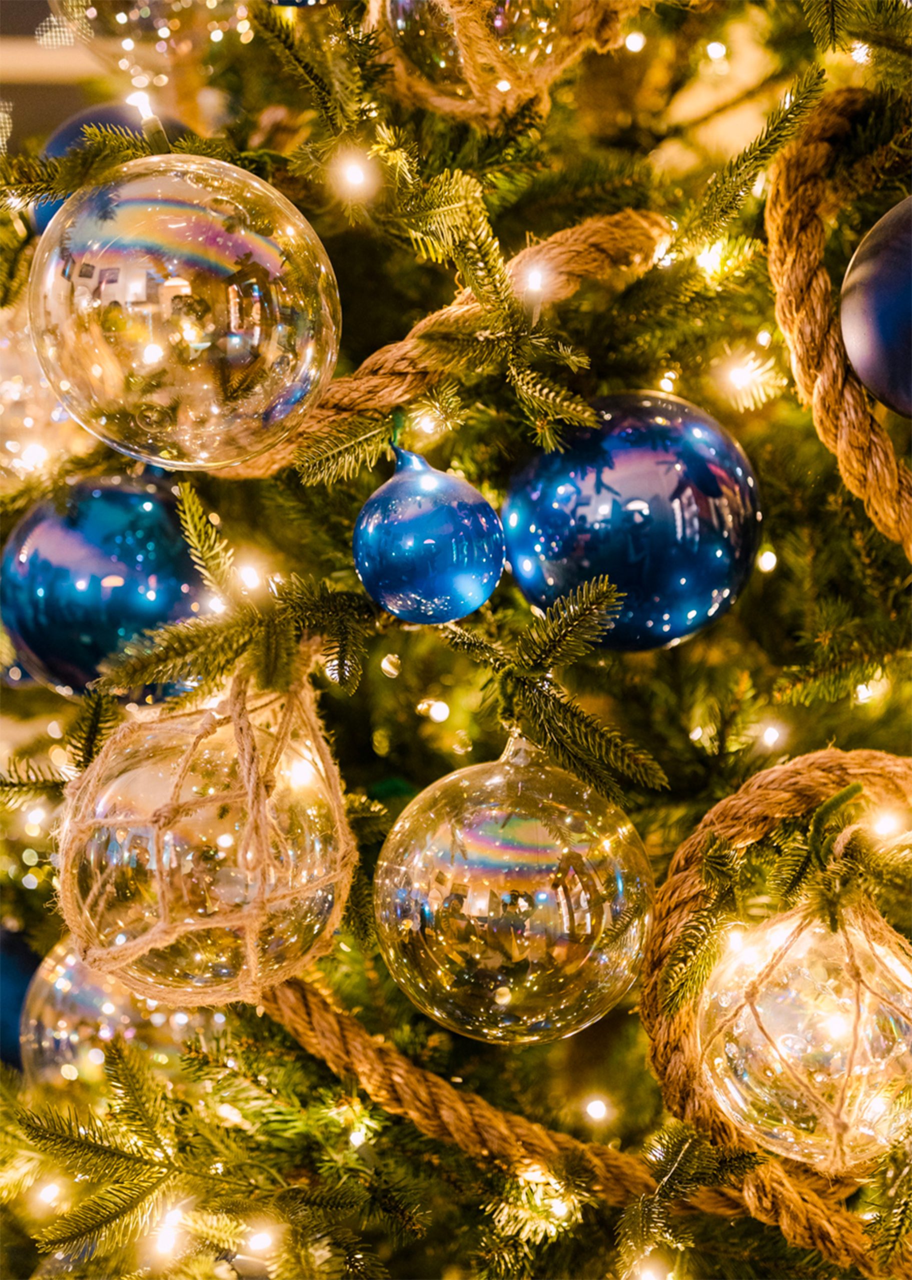Dettaglio albero di Natale decorato con sfere blu e trasparenti, luci calde e corda. Decorazioni natalizie eleganti per feste e celebrazioni. Design natalizio con addobbi di lusso.